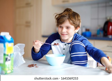 Happy little blond kid boy eating cereals for breakfast or lunch. Healthy eating for children. Child in colorful pajama having breakfast with milk and muesli.