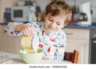 Happy little blond kid boy eating cereals for breakfast or lunch. Healthy eating for children in the morning. Child in colorful pajama nightwear having breakfast with milk and oat granola muesli - Powered by Shutterstock