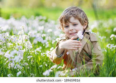 Happy little blond toddler boy in spring garden with blooming white flowers, outdoors.