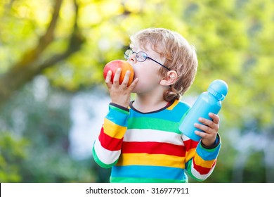 Happy little boy with books, apple and drink bottle on his first day to elementary school or nursery. Outdoors.  Back to school, kids, lifestyle concept. Child eating fruit