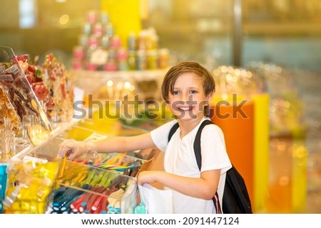 happy little boy in a candy store chooses sweets, marmalade candies, puts them in a paper bag