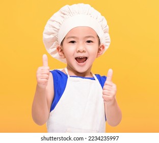 Happy little boy in chef uniform showing thumbs up on yellow background - Powered by Shutterstock