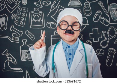 Happy Little Boy In Doctor Costume Lifts Thumbs Up On Dark Background With Pattern. The Child Has Mustache And Glasses.