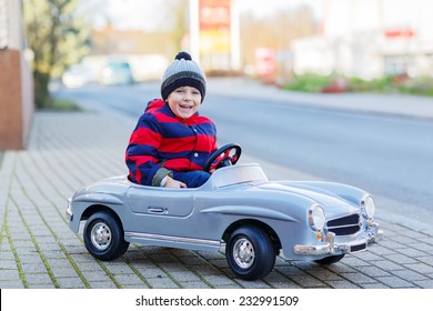 Happy Little Boy Driving Big Vintage Old Toy Car And Having Fun, Outdoors. Kids Leisure On Cold Day In Winter, Autumn Or Spring.