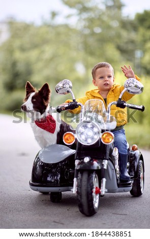Happy little boy driving a toy motorcycle with his dog in a park