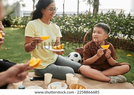 Happy little boy eating orange at family picnic