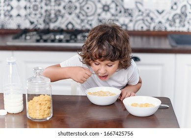 Happy little boy eats with pleasure healthy breakfast of cornflakes and milk at the kitchen.