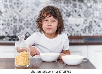 Happy little boy eats with pleasure healthy breakfast of cornflakes and milk at the kitchen.