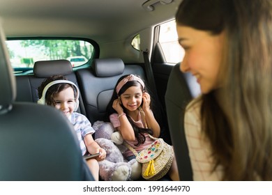 Happy Little Boy And Girl With Headphones Watching A Movie On A Tablet While Sitting In The Car. Fun Young Woman Driving With Her Cute Kids 