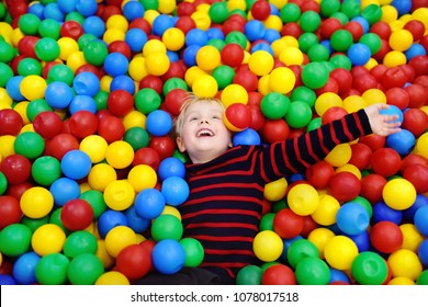 Happy little boy having fun in ball pit with colorful balls. Child playing on indoor playground. Kid jumping in ball pool.