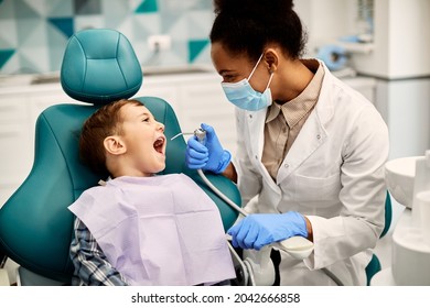 Happy little boy having his teeth checked by female dentist during appointment at dental clinic. 
