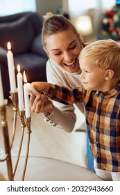 Happy Little Boy And His Mother Lighting Up Candles In Menorah On Hanukkah At Home.