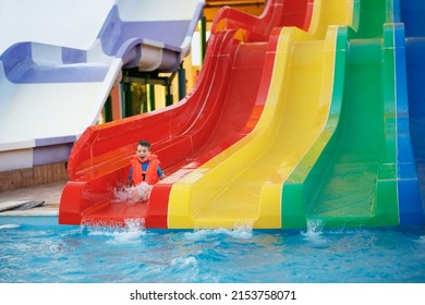 happy little boy in inflatable vest on water slide at aquapark. Summer holiday concept