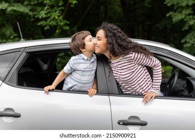 Happy little boy kissing millennial mom in open car window, outdoor in summer, free space. Traveling on weekend with child, family enjoy vacation together, road and vacation together, journey by auto
