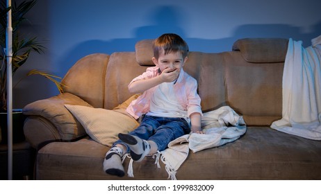 Happy Little Boy Laughing On Funny TV Show Or Comedy Movie At Night