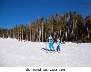 Happy Little Boy Learns To Ski With His Father During Winter Holidays In Snowy Mountains On A Sunny Cold Day. An Interesting Active Holiday With The Family. Healthy Lifestyle, Enjoy The Moment