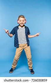 happy little boy listening music in headphones and dancing isolated on blue
