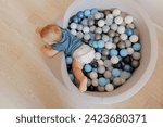 Happy little boy play in dry pool with colorful balls in living room, aerial top view. Concept lifestyle childhood moment.