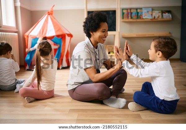 Happy little boy\
playing clapping game with African American PE teacher on exercise\
class at kindergarten. 