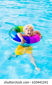 Happy little boy playing with colorful inflatable ring in outdoor swimming pool on hot summer day. Kids learn to swim. Child water toys. Children play in tropical resort. Family beach vacation
