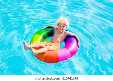 Happy little boy playing with colorful inflatable ring in outdoor swimming pool on hot summer day. Kids learn to swim. Child water toys. Children play in tropical resort. Family beach vacation