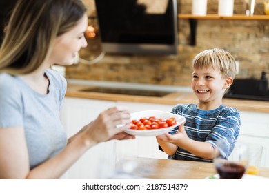 Happy little boy serving  food to his mother at dining table - Powered by Shutterstock