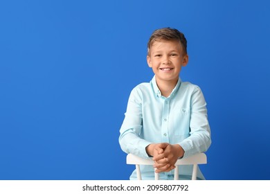 Happy Little Boy Sitting In Chair On Blue Background