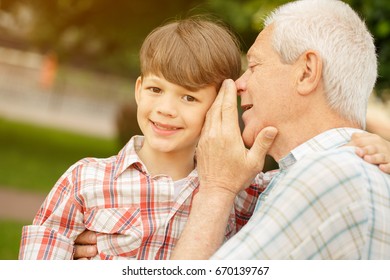 Happy little boy smiling to the camera while his grandpa whispering secrets to his ear outdoors people children family retirement parents love trust communication gossip news emotions parenthood - Powered by Shutterstock