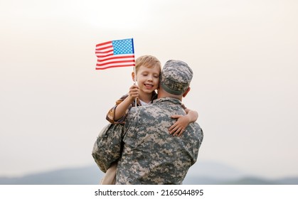 Happy little boy son with American flag hugging father in military uniform came back from US army, rear view of male soldier reunited with family while standing in green meadow on summer day - Powered by Shutterstock