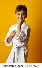 Happy little boy in white kimono of fighter standing in stance smiling at camera on yellow background