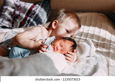 Happy little brother with newborn baby lying in a bed together, kissing and hugging. Siblings. New born baby and three years old brother together. Love. Family. - Powered by Shutterstock