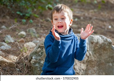 Happy Little Caucasian Boy With Sitting On Rocks And Clapping Hands Of Joy. Happy Little Child Stock Image. Weekend Coming, Happy Family Event