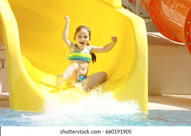 Happy Little Caucasian Girl On Waterslide Of Water Park. Summer Sunny Day.