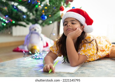 Happy Little Caucasian Girl Thinking About Christmas Wish List. She Is At Home Lying On The Carpet.
