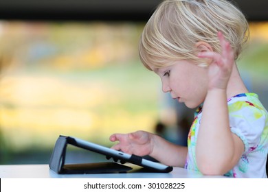 Happy Little Child, Adorable Blonde Toddler Girl Enjoying Modern Generation Technologies Playing Indoors Using Tablet Pc With Touchscreen.