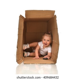 Happy Little Child Baby Girl Hiding In A Cardboard Box Having Fun Laughing Smiling With Mobile Cellphone Isolated On A White Background