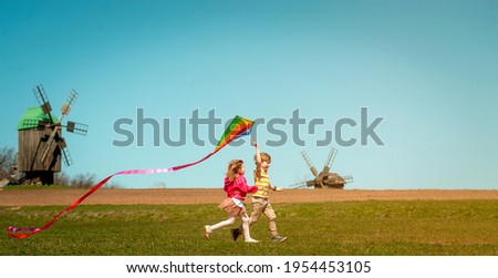 Happy little child girl and boy in front of windmills playing kite. Children running on the field. Renewable and green energy. Kids playing near a wind turbine. New generation