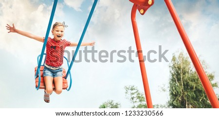 Happy little child girl laughing and swinging on a swing in the city park in summer 