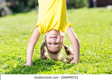Happy little child girl standing on her head on green lawn.
