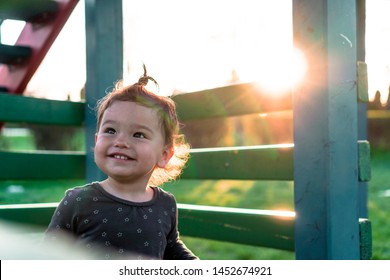 Happy Little Child Playing Outdoors On Jungle Gym At Sunset. Laughing Kid Standing On Kids Playground Outside In Nature On Sunny Day. Smiling Toddler Looking Up Backlit By Sunshine. 