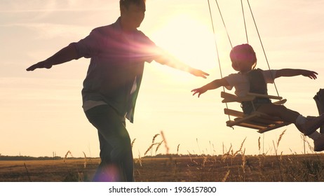 Happy Little Child With A Teddy Bear And Dad Is Riding A Swing At Sunset In The Park, Playing The Plane Flying In The Air. Daughter And Father Are Having Fun At Dawn. Happy Family Life Concept. Kid