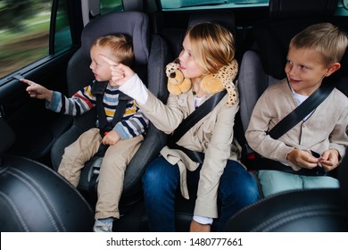 Happy little children boys and their sister are sitting in their safety chairs, riding in family car. Saloon view. All looking at something interesting outside, pointing with their fingers - Powered by Shutterstock