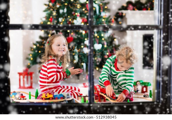 Happy little children in matching pajamas playing with\
Christmas presents - wooden toy railroad and car. Family Xmas\
morning in decorated living room with kids gifts, fireplace and\
Christmas tree. 