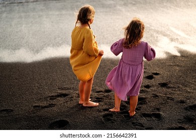 Happy Little Cute Girls Enjoying Sunny Day At The Beach, Standing On The Coast And Looking At The Waves. Family Summer Vacation. Sister's Love. A Lot Of Copy Space.
