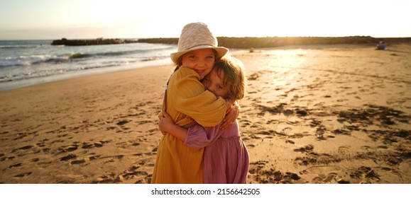 Happy Little Cute Girls Enjoying Sunny Day At The Beach, Hugging And Smiling To The Camera. Family Summer Vacation. Sister's Love. A Lot Of Copy Space.
