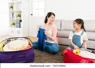 happy little daughter with beauty mother looking each other when they sitting in living room packing travel luggage suitcase together.
