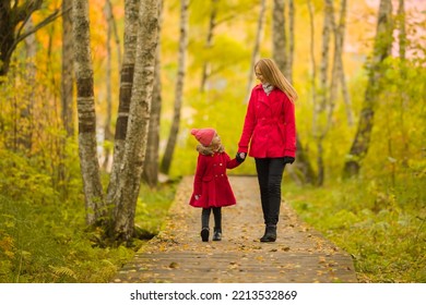 Happy little daughter and young adult mother walking on trail at birch tree forest. Spending time together in beautiful colorful autumn day. Enjoying stroll. Front view. - Powered by Shutterstock