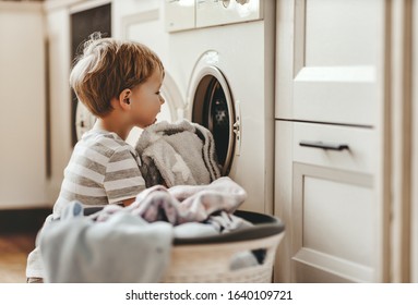 happy little funny householder child boy in laundry   with washing machine