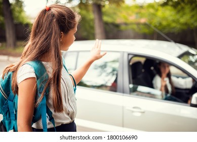 Happy little girl with backpack waving goodbye to her mother. Young parent gave her daughter a lift to the school and farewells to her - Shutterstock ID 1800106690