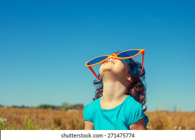 Happy little girl with big sunglasses looking at the sky